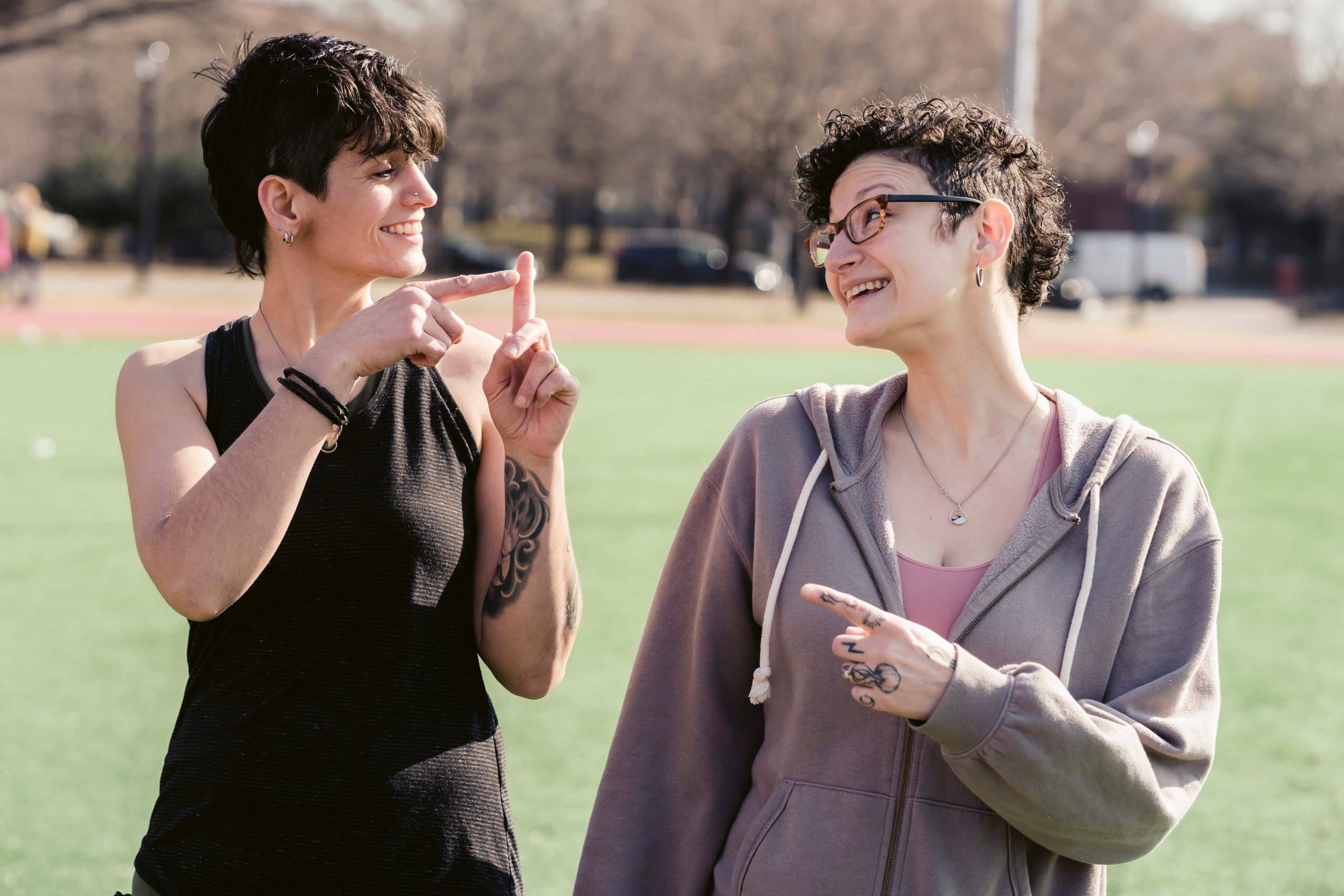 two ladies in a park, they are using sign language to talk to each-other. They are discussing BSL Counselling.