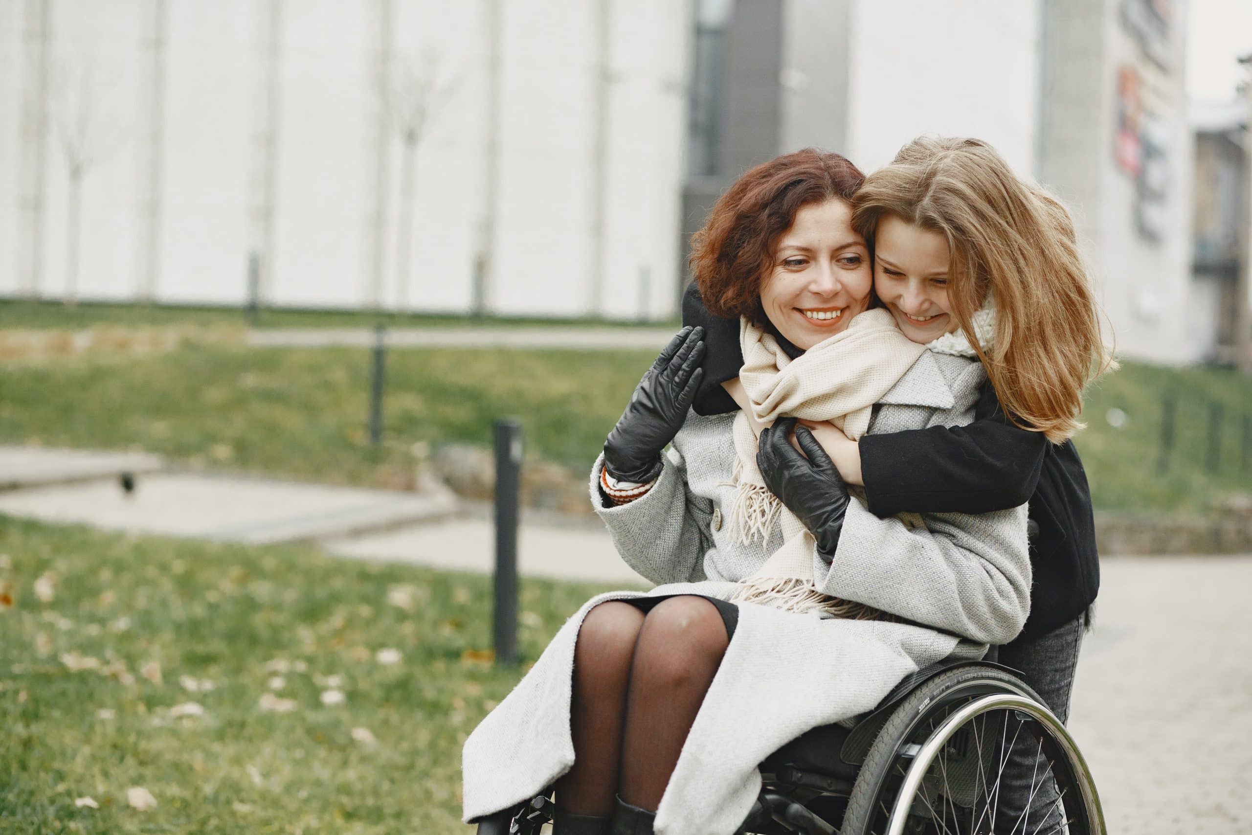 Lady in a wheelchair, she is being hugged by a family member. The lady in the wheelchair is explaing how much her Parkinson's Disease counselling is helping her.