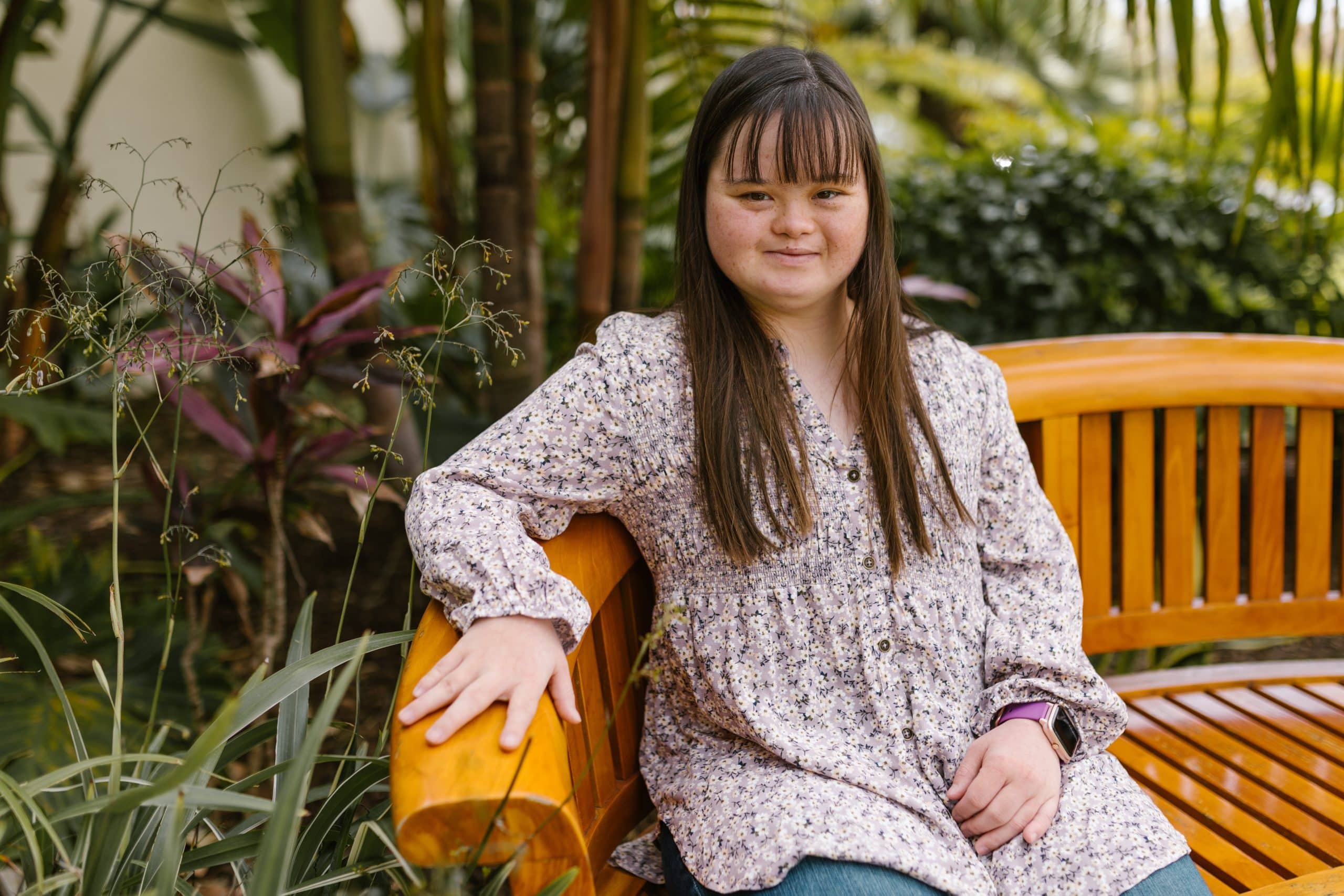 A lady sat on bench in a park, she is happy she started Down's Syndrome Counselling