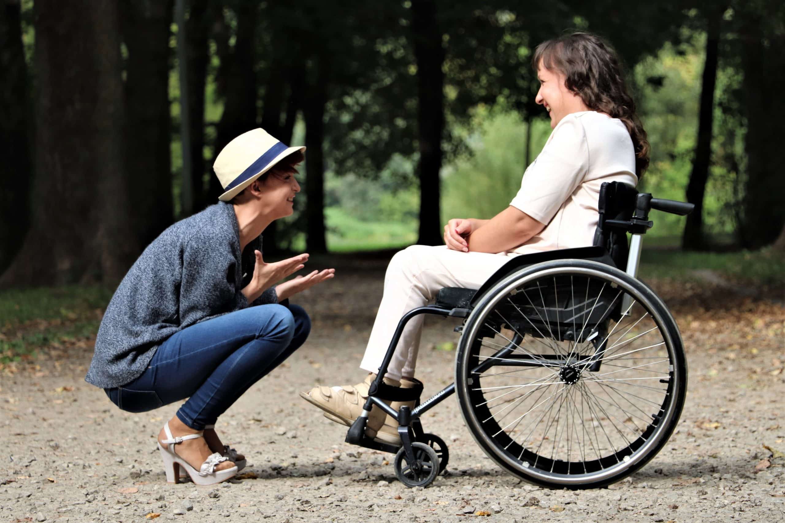 A man with a hat on crouched down looking at a lady in a wheelchair. He is explains how counselling for carers has helped him.