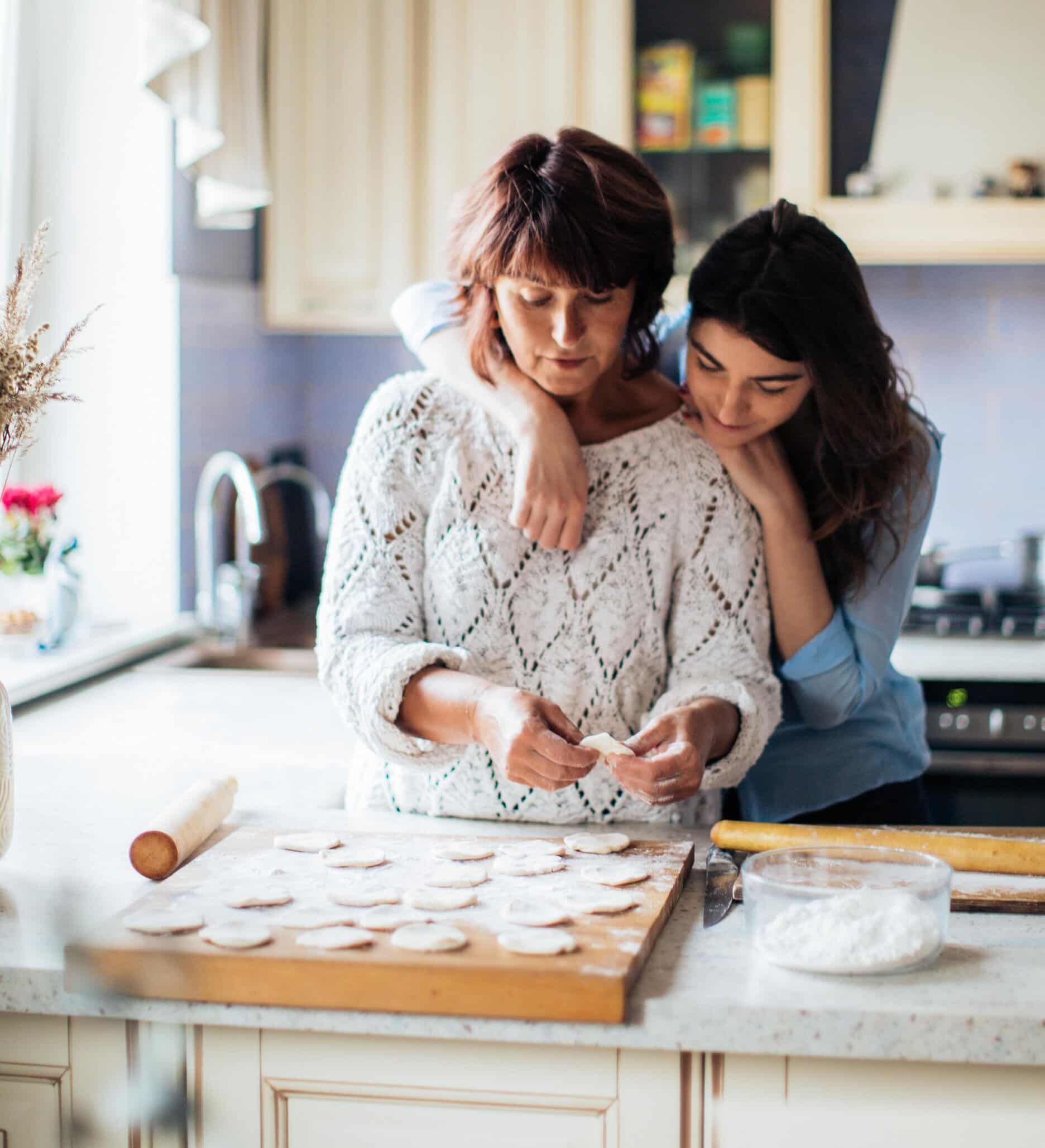 A lady stood in the kitchen making some cakes, her daughter is stood behind her smiling as her mother has started tinnitus counselling.