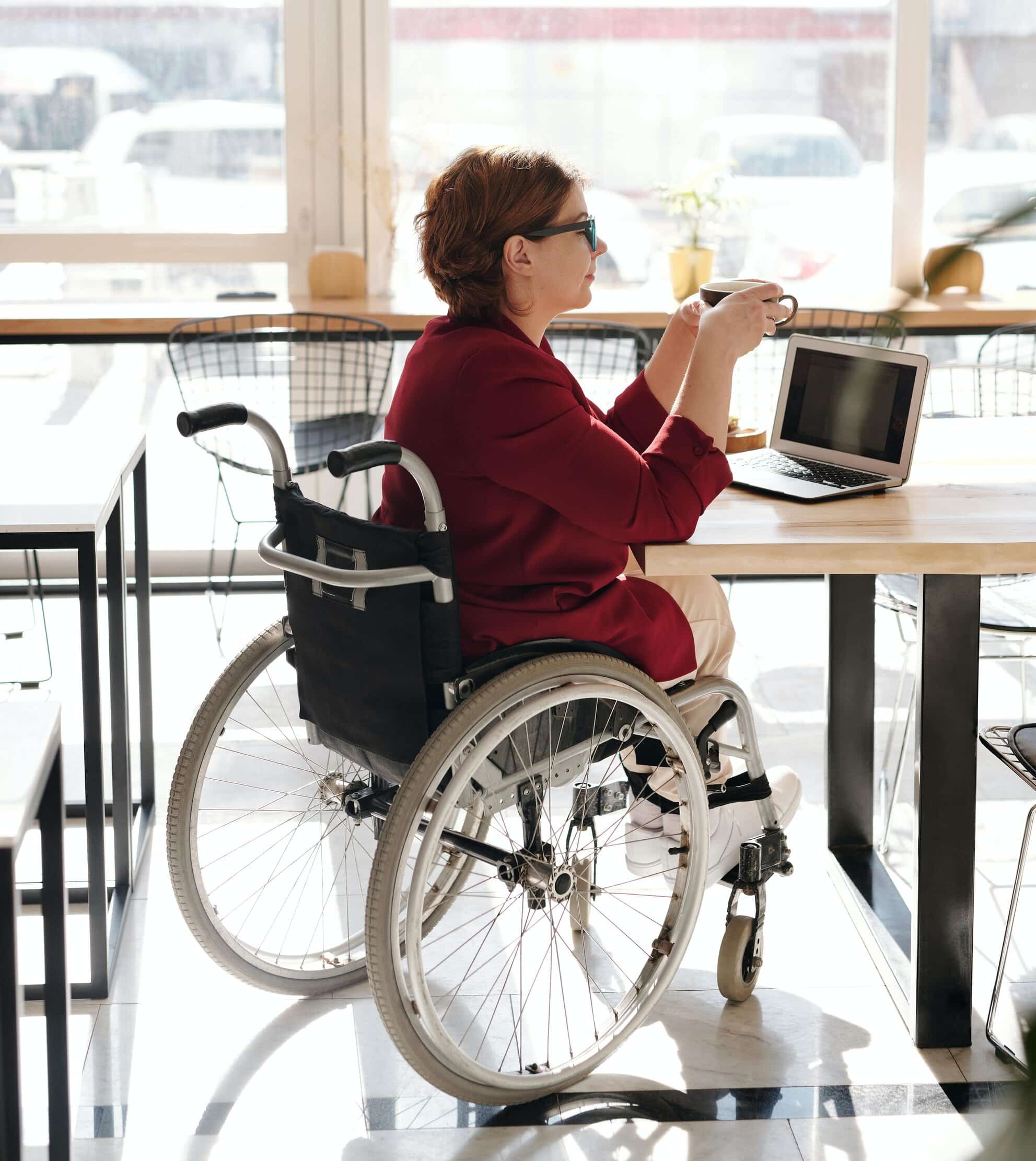 A couple sat in their wheelchairs on paving, they are looking at a church with many people walking towards them. They are feeling better after having spinal cord injury counselling