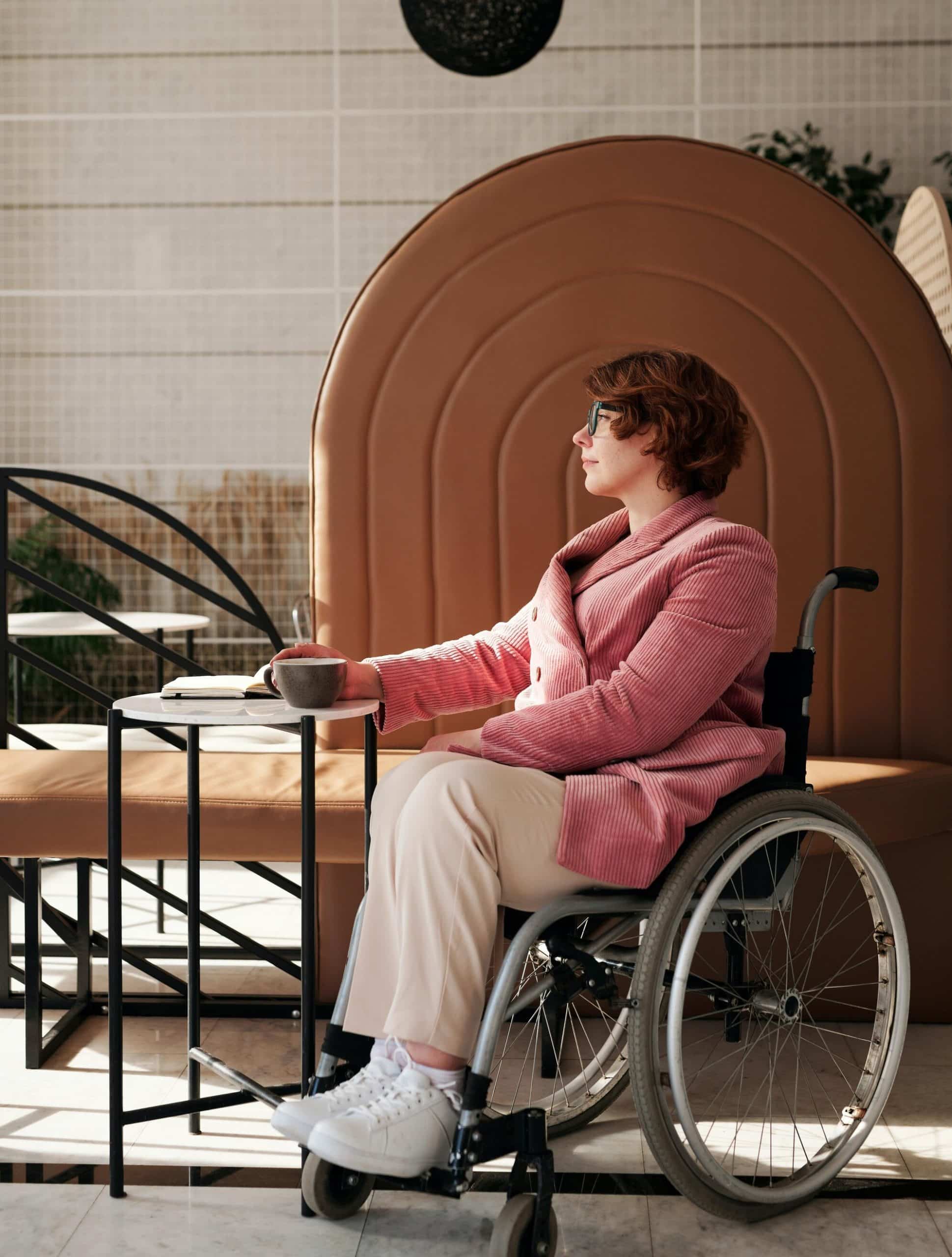 Lady sat in her wheelchair, she is in her kitchen stroking her cat.