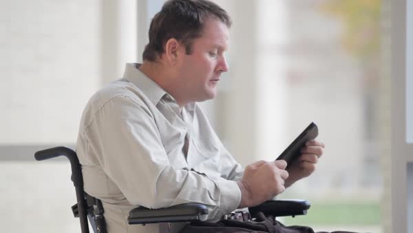 A couple sat in their wheelchairs on paving, they are looking at a church with many people walking towards them. They are feeling better after having spinal cord injury counselling