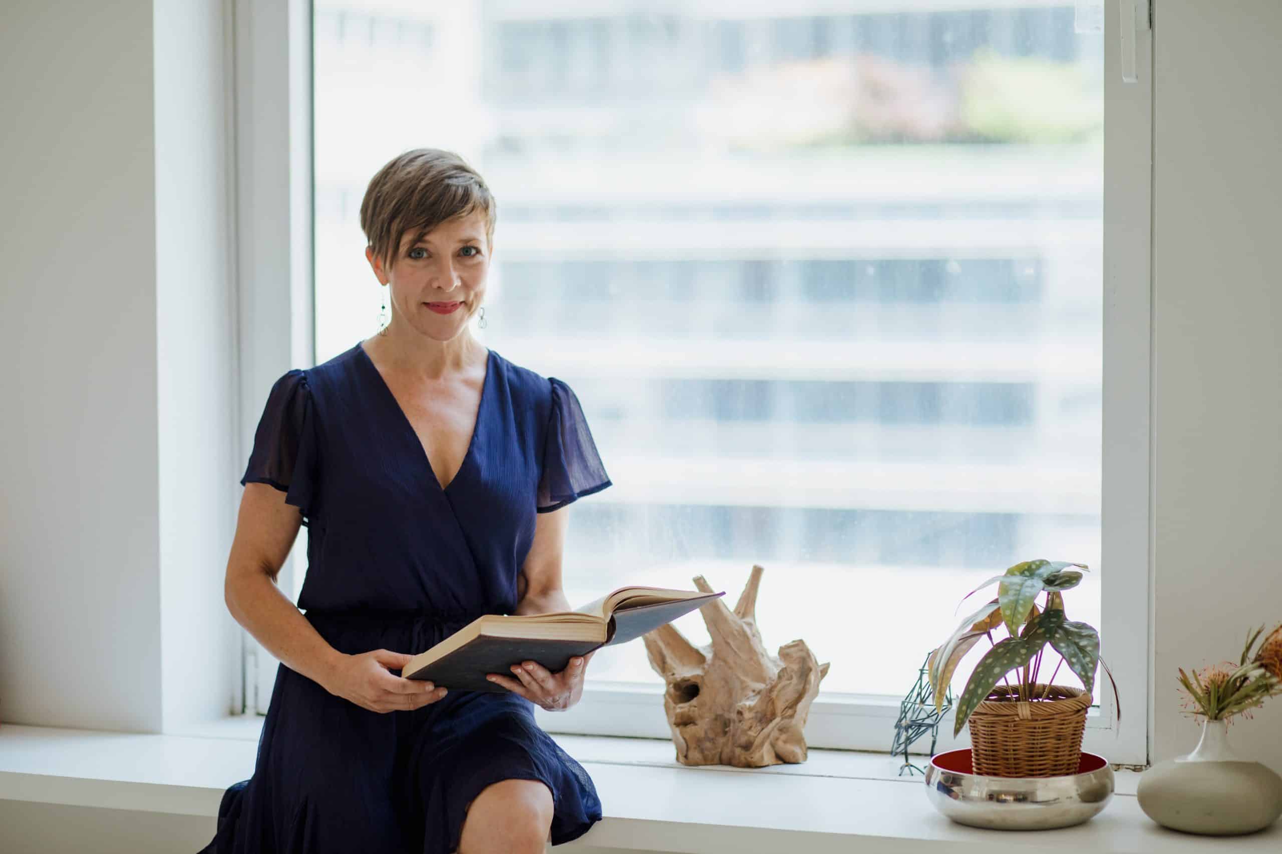 Therapist sat on a window ledge holding a book. She is looking at her appointments for ASD Counselling this week.